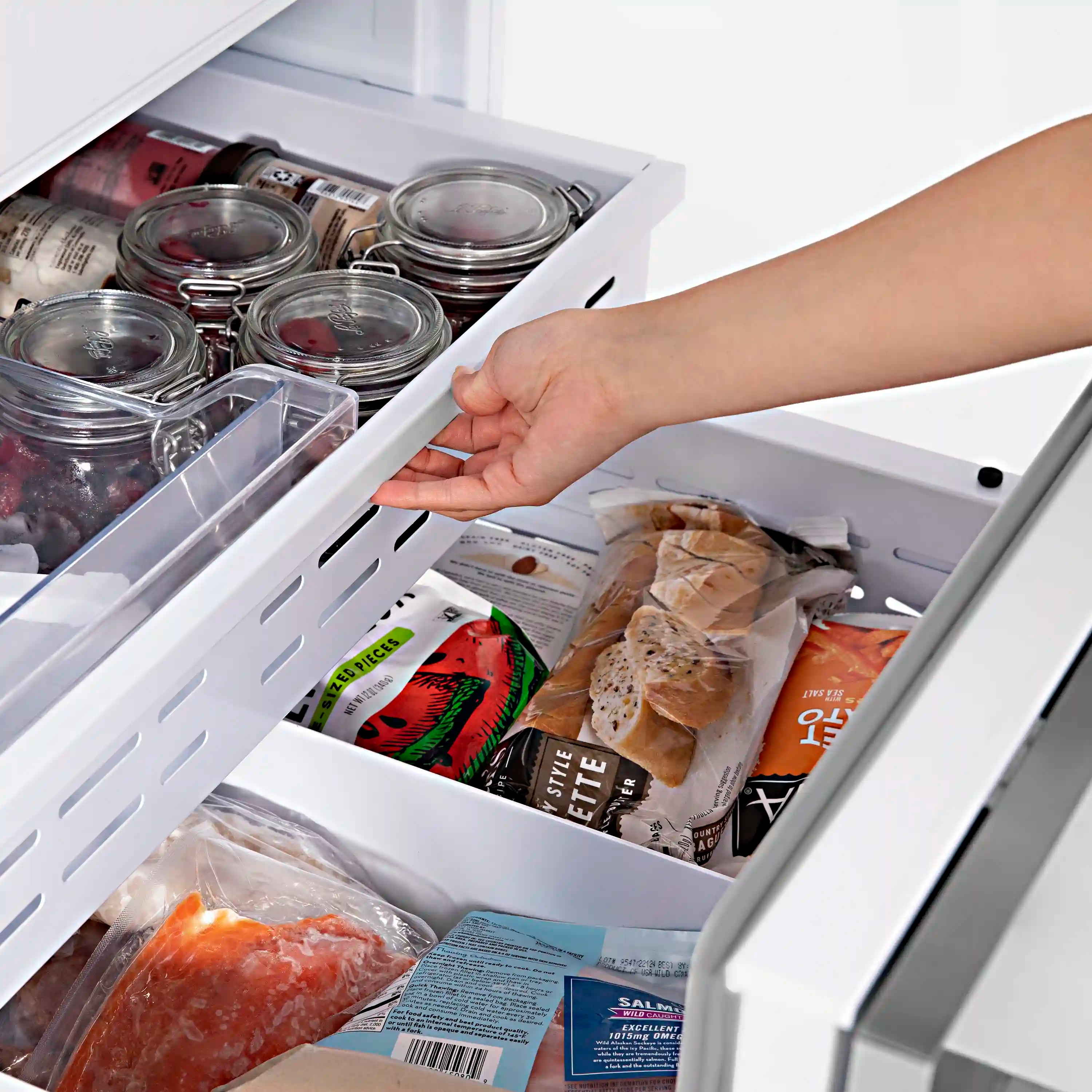 Bottom freezer drawer open with shelves and a hand reaching in
