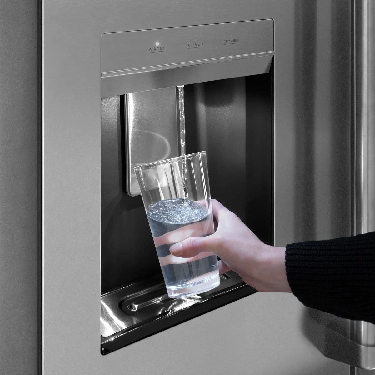 External water dispenser dispensing water into a glass cup on a stainless steel refrigerator