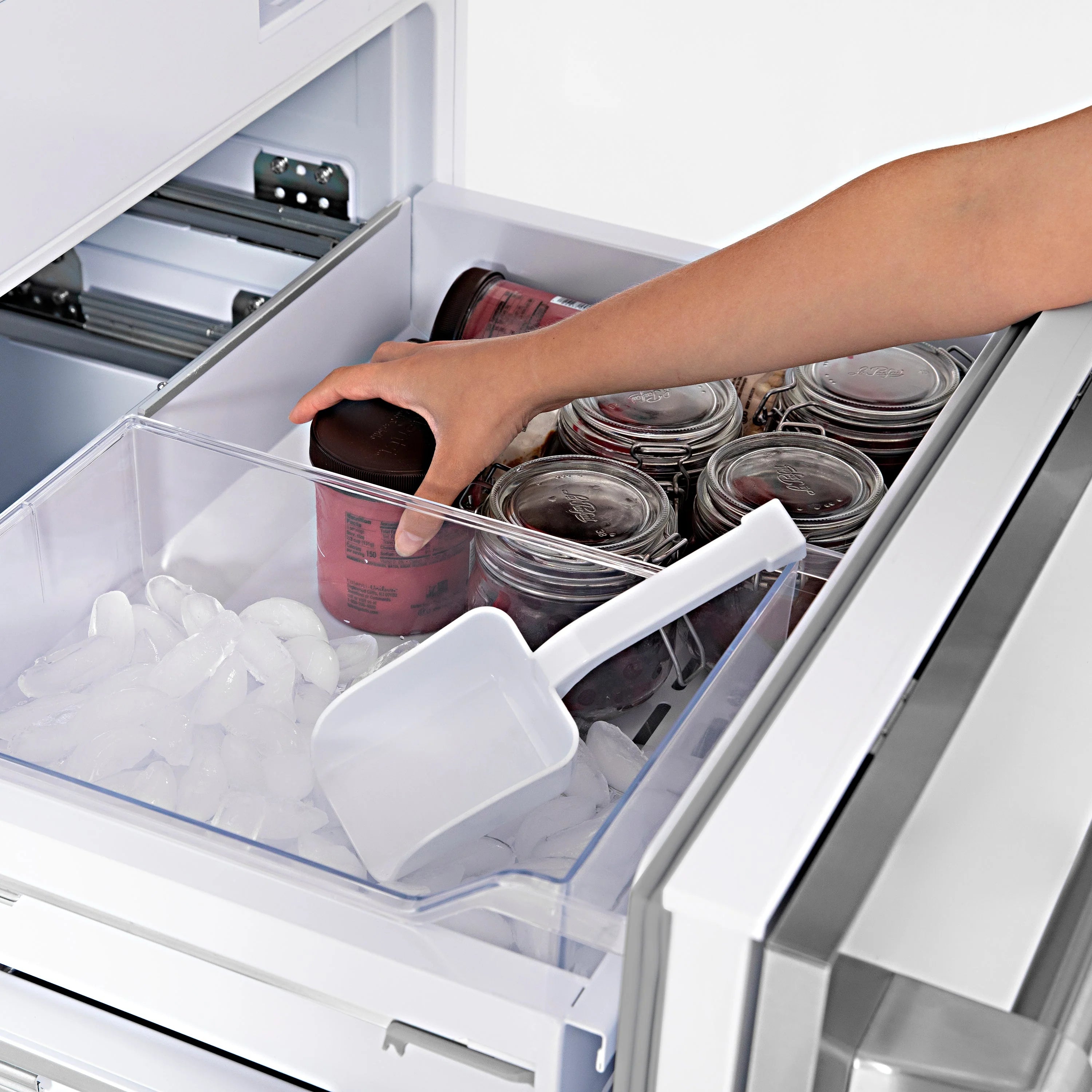 Open freezer bin with jars and ice tray, hand reaching inside