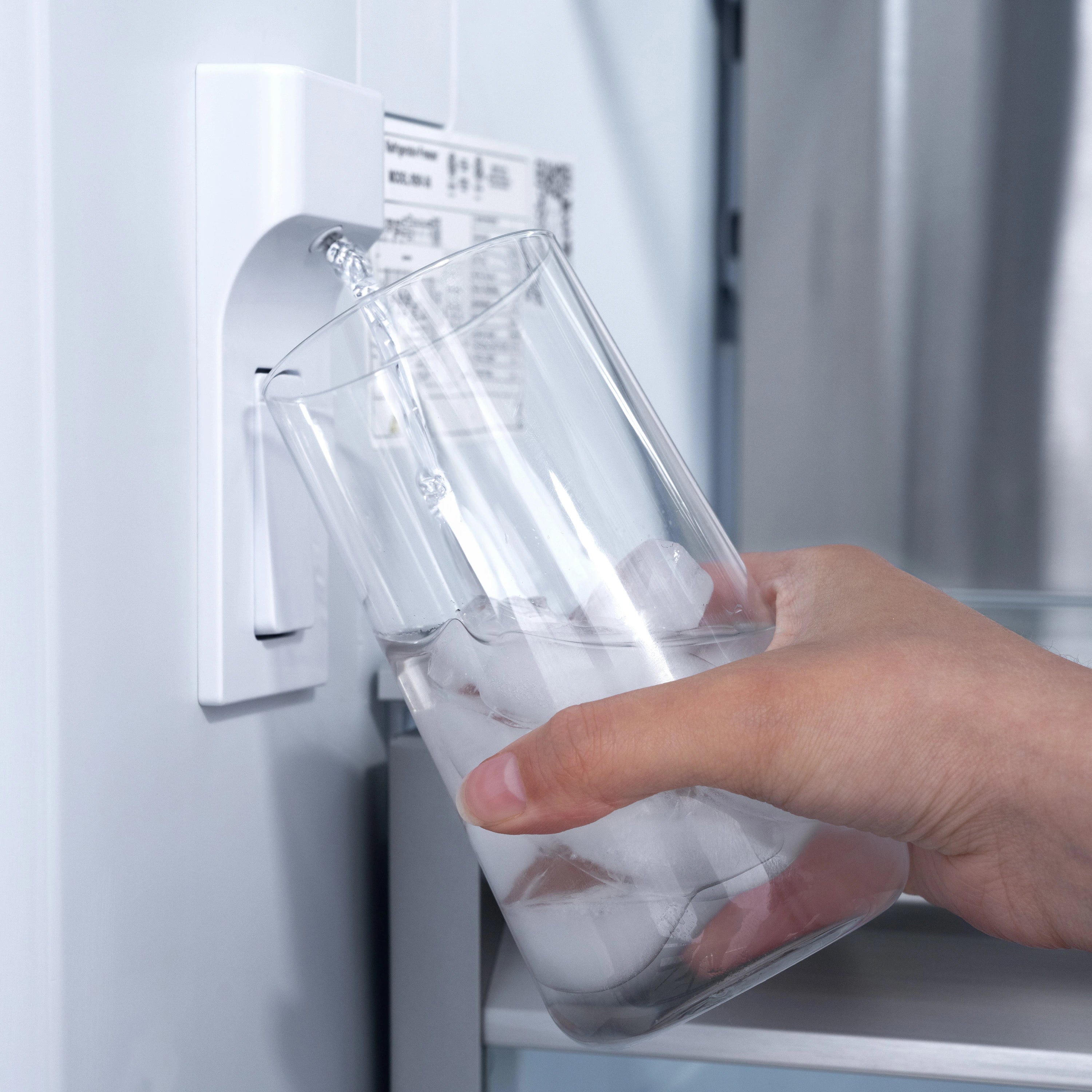 White water dispenser filling a clear glass with ice cubes