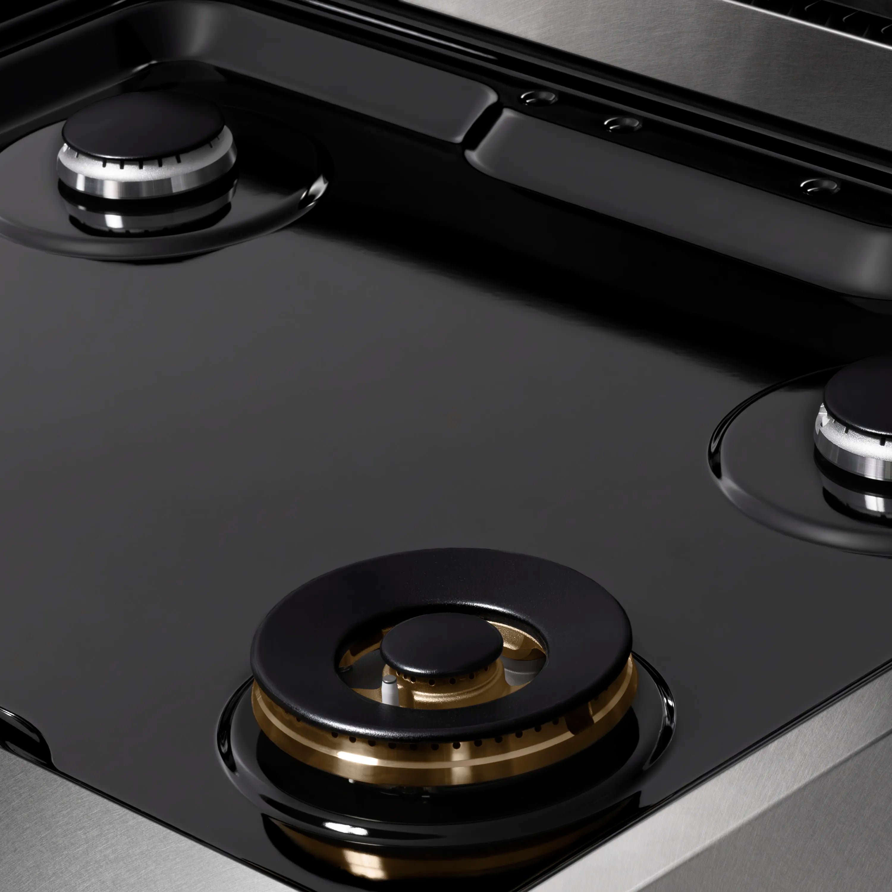 Close-up gas burner head with black cap and brass ring on dark cooktop
