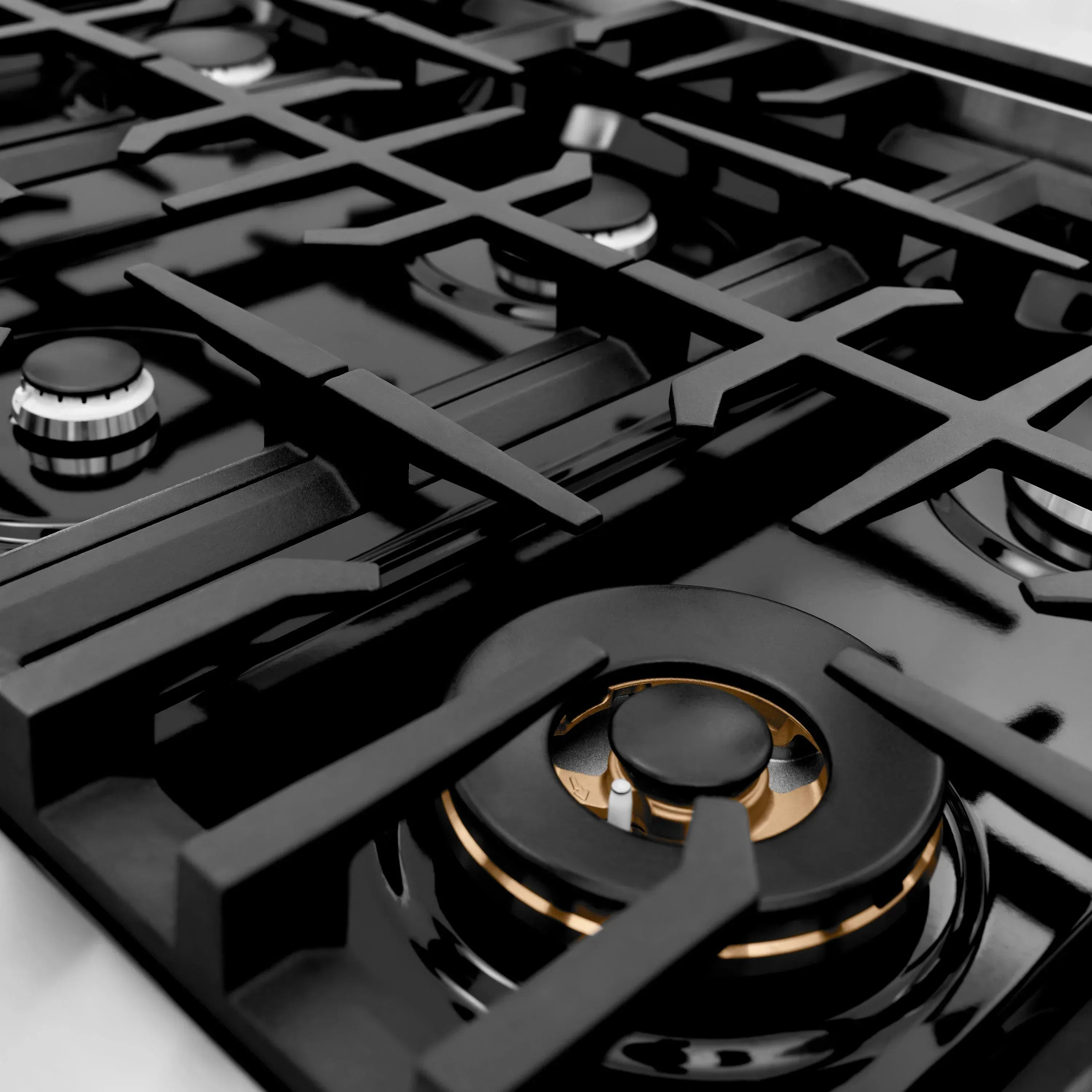 Close-up of black gas burner grates with gold ring on stainless cooktop