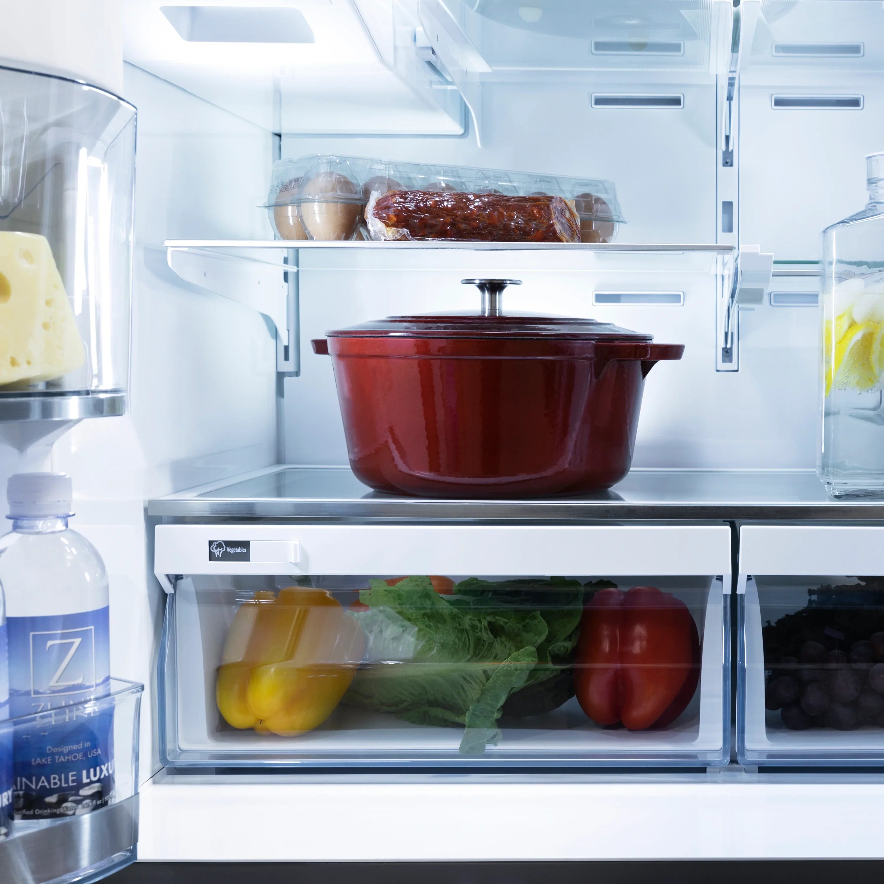 Refrigerator interior with red cookware and produce in glass shelves