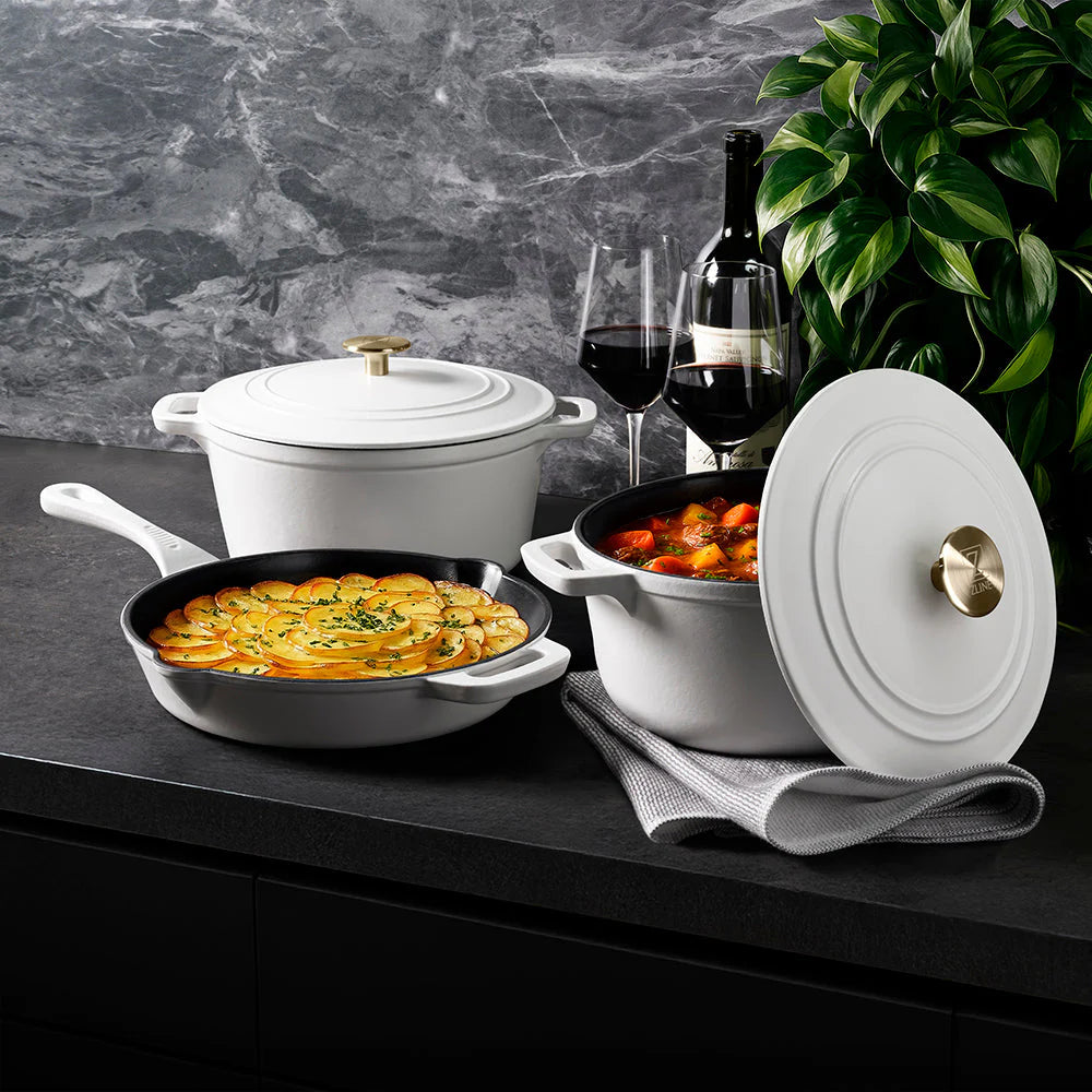 White matte enameled cast iron cookware with covered pot and black skillet, gold knobs
