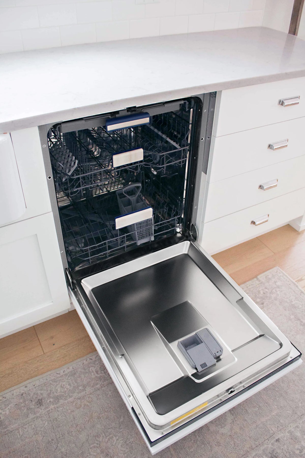 Built-in dishwasher door open with stainless interior tub and empty racks
