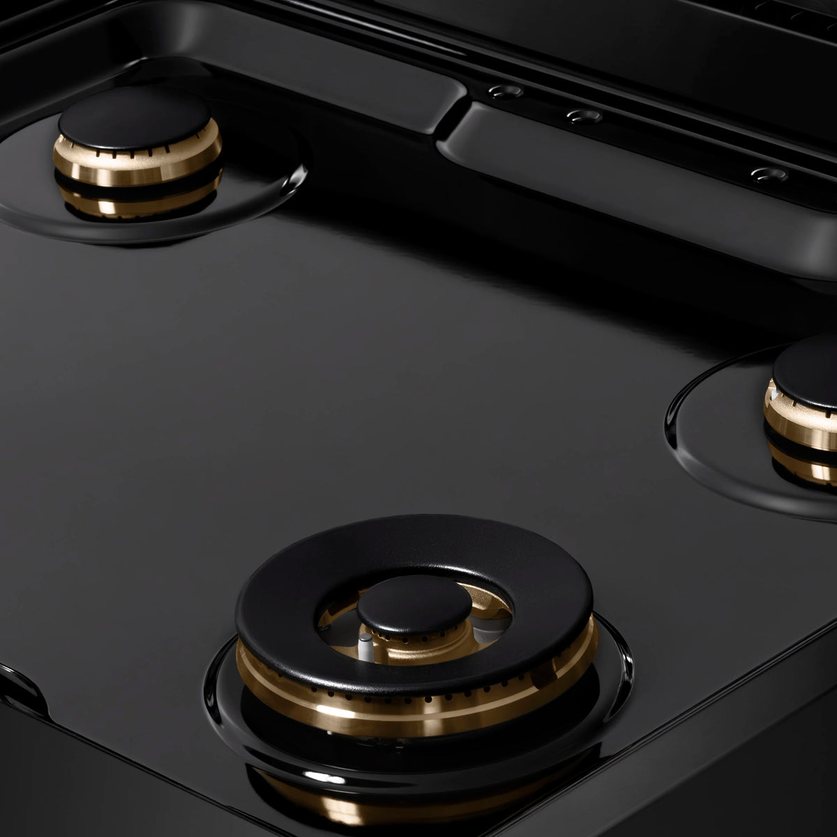 Black gas rangetop showing three brass-trim burners with black burner caps