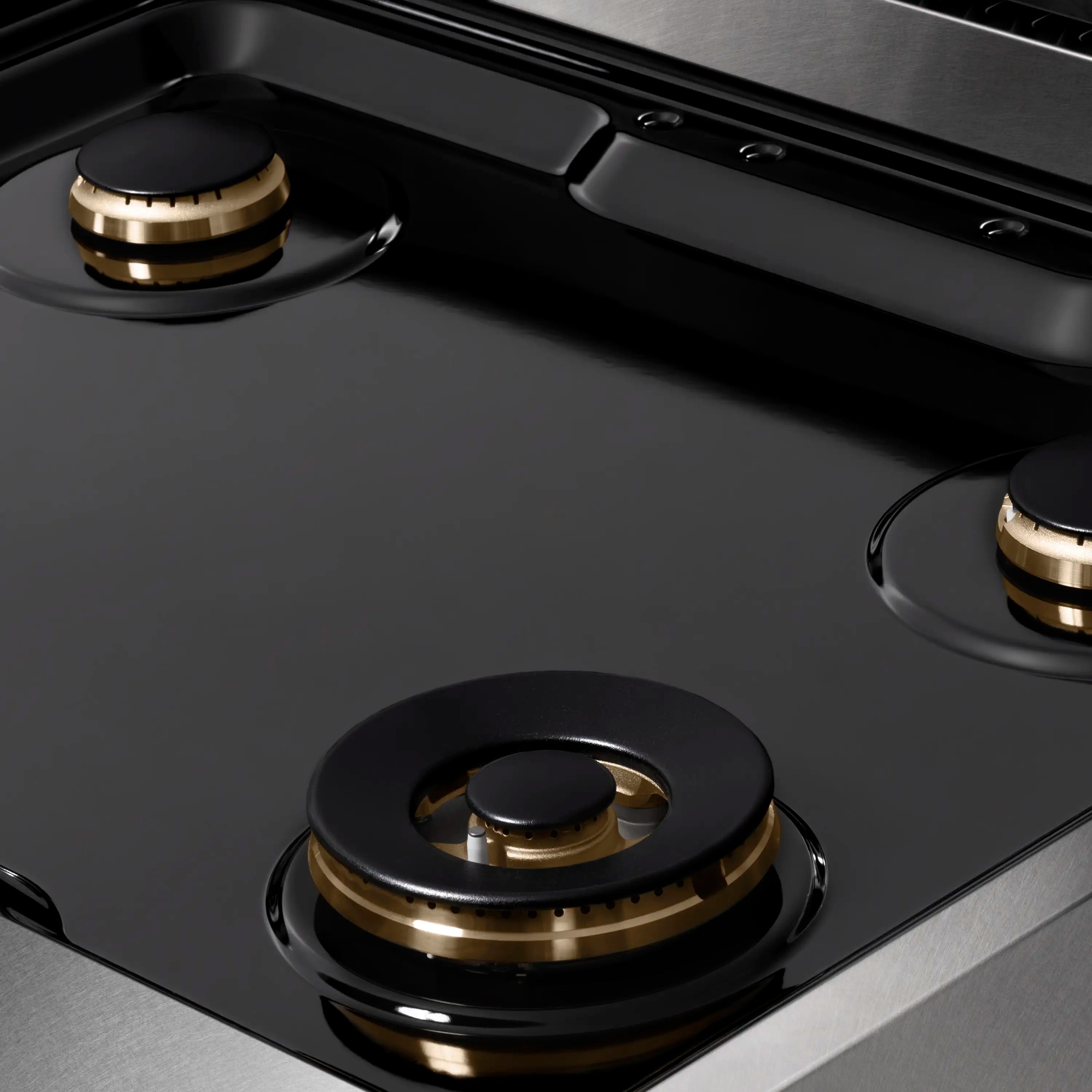 Gas cooktop surface with black burner caps and brass trim on satin stainless steel