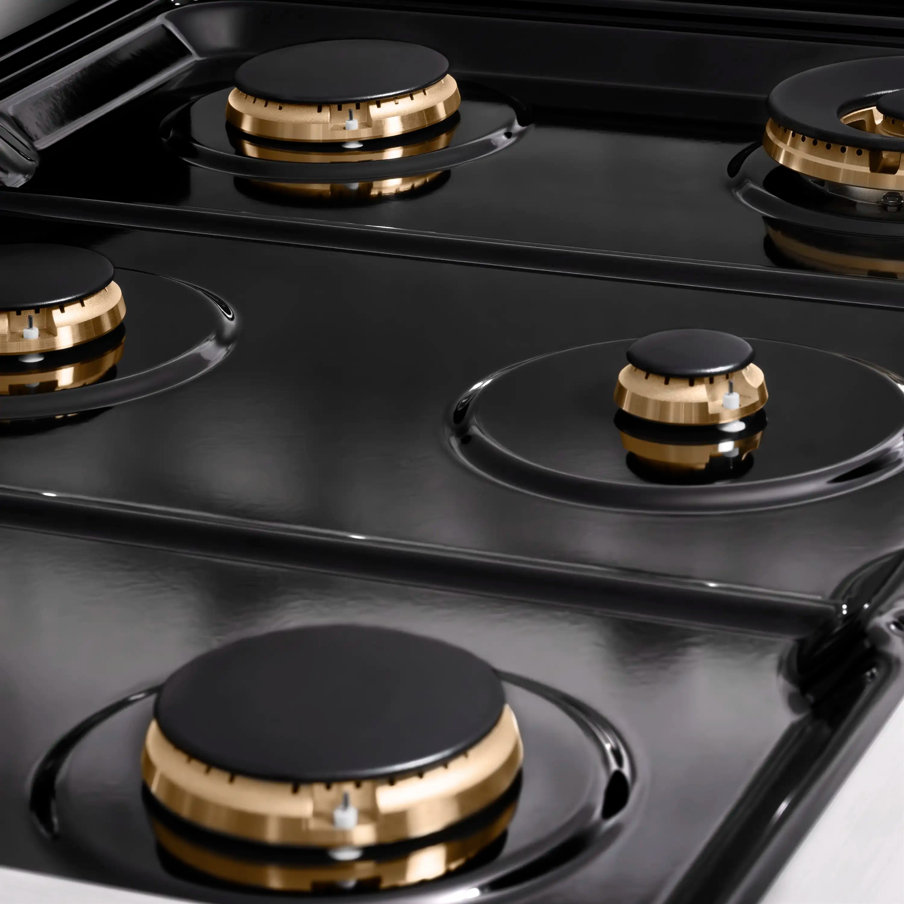 Black gas cooktop surface with four round burner caps and brass rings