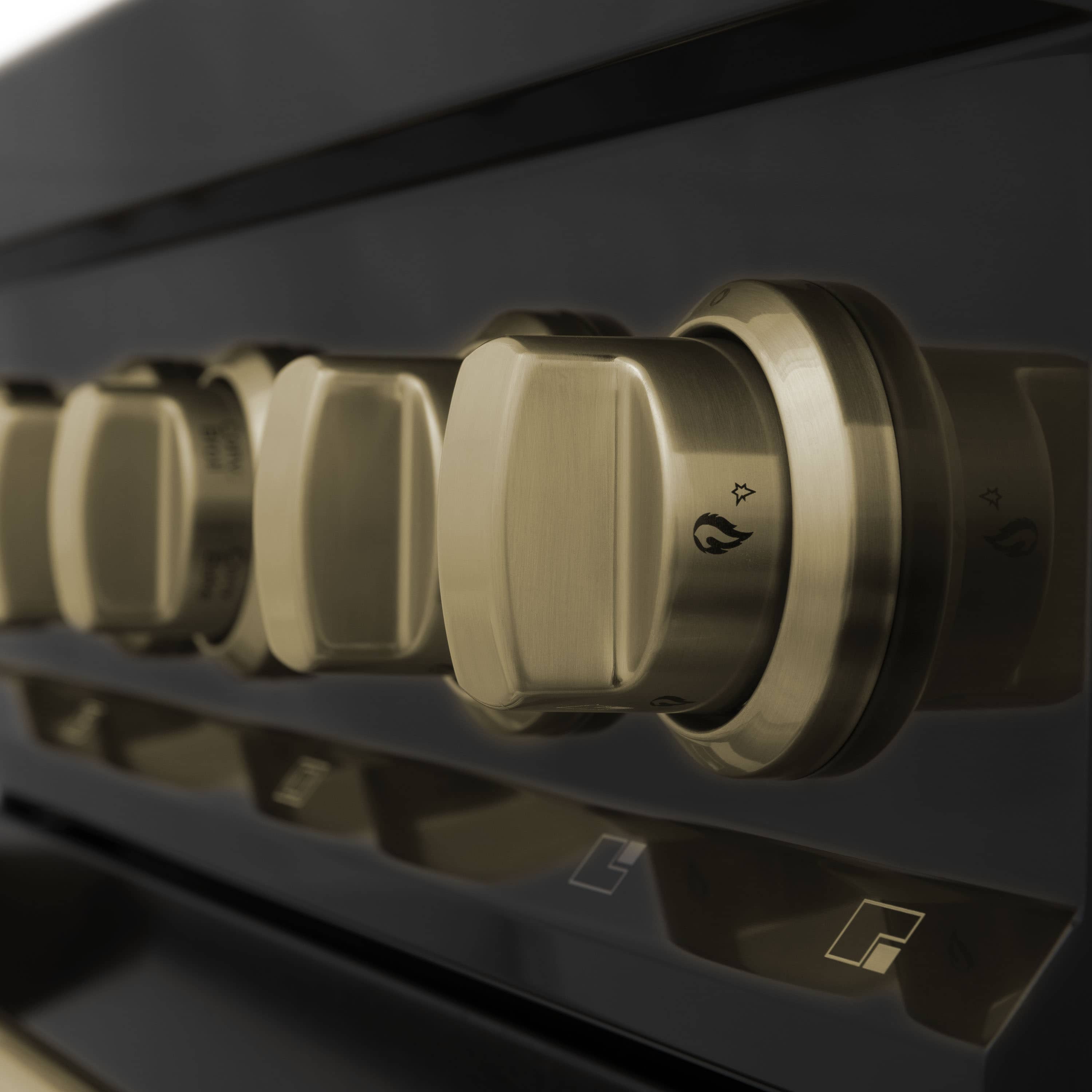 Close-up of brass-tone range knobs and burner icons on dark control surface