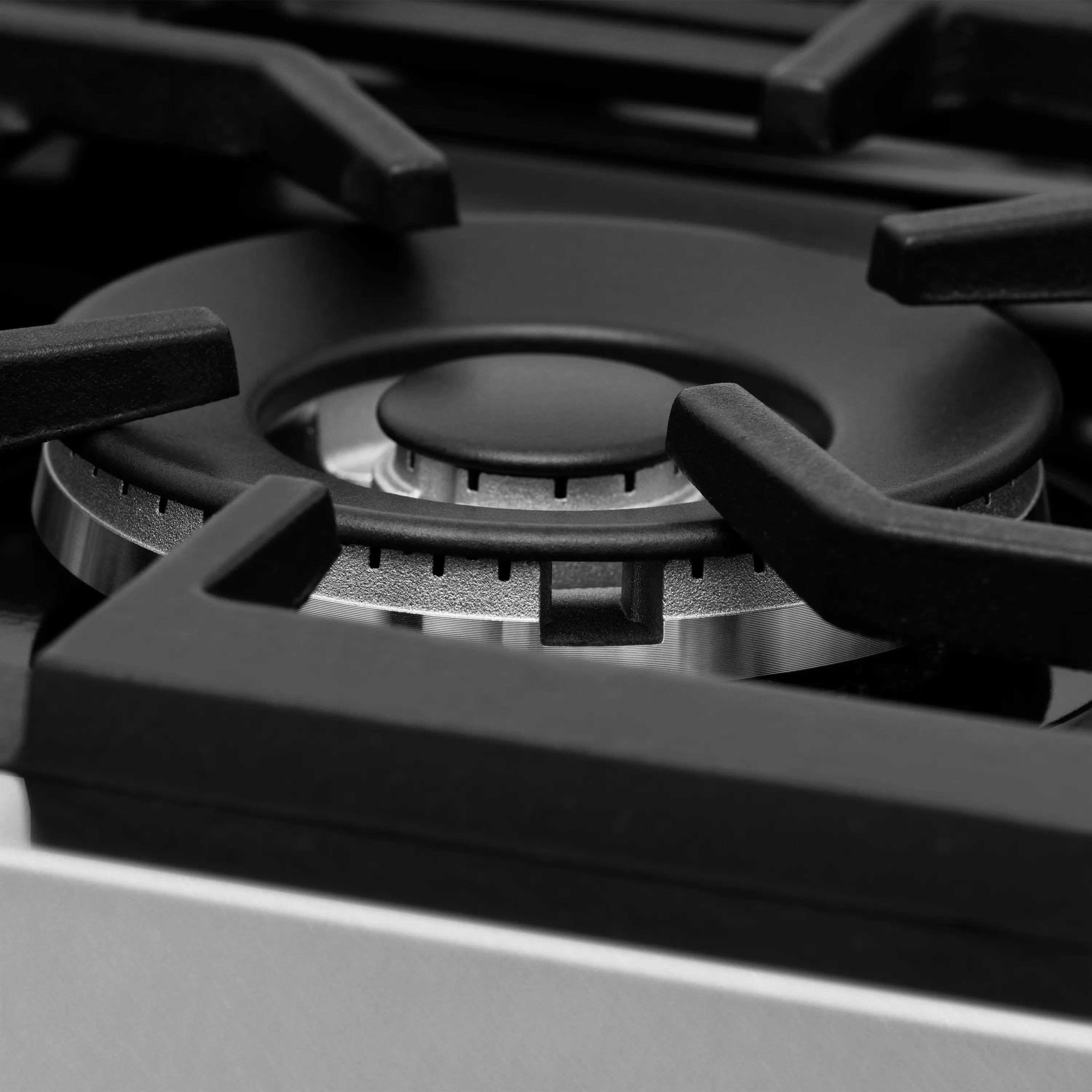 Gas stovetop burner with black grate and round metal control cap, close-up