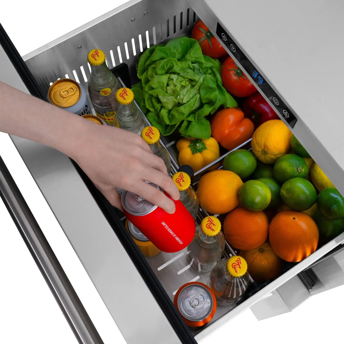 Outdoor refrigerator drawer with produce and bottles, hand reaching for a red can