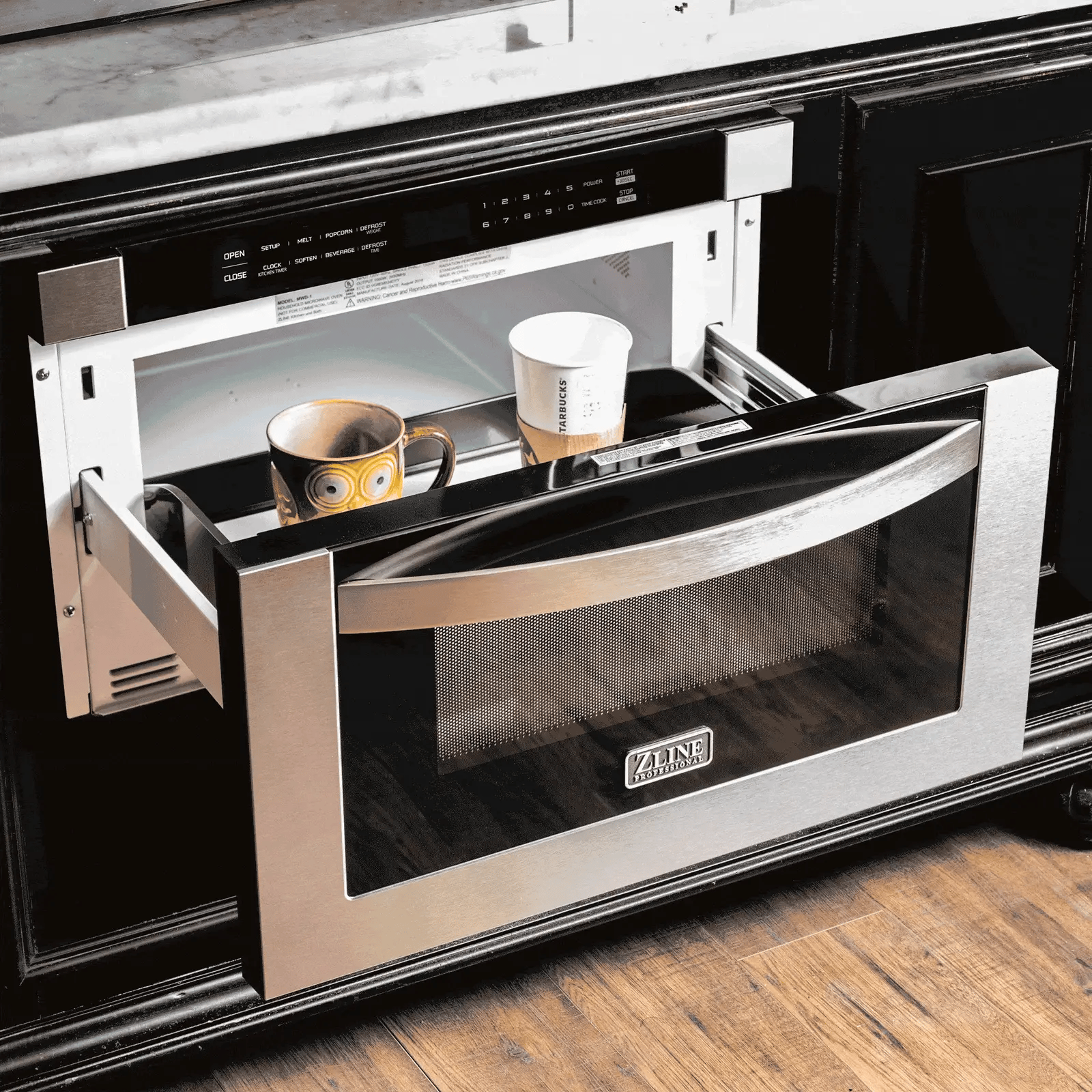 Microwave drawer open showing mugs and cookware inside