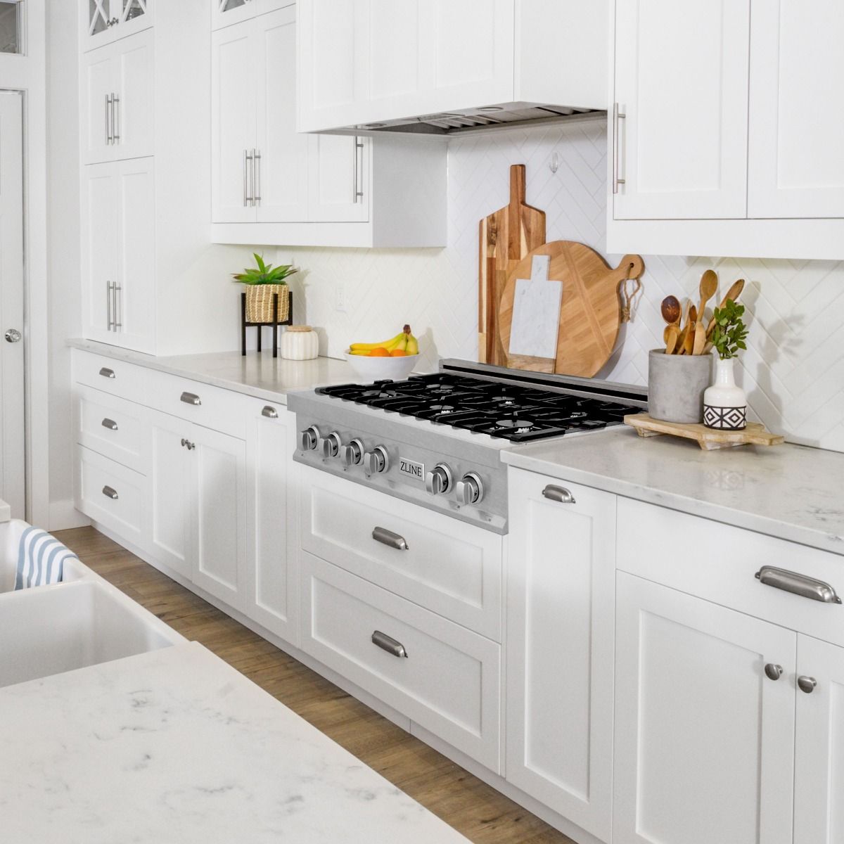 Stainless steel gas range with black burner grates and control knobs under a hood