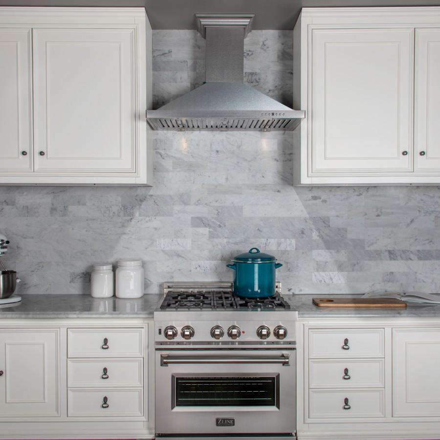 Satin stainless steel range hood over gas cooktop, mounted between white cabinets