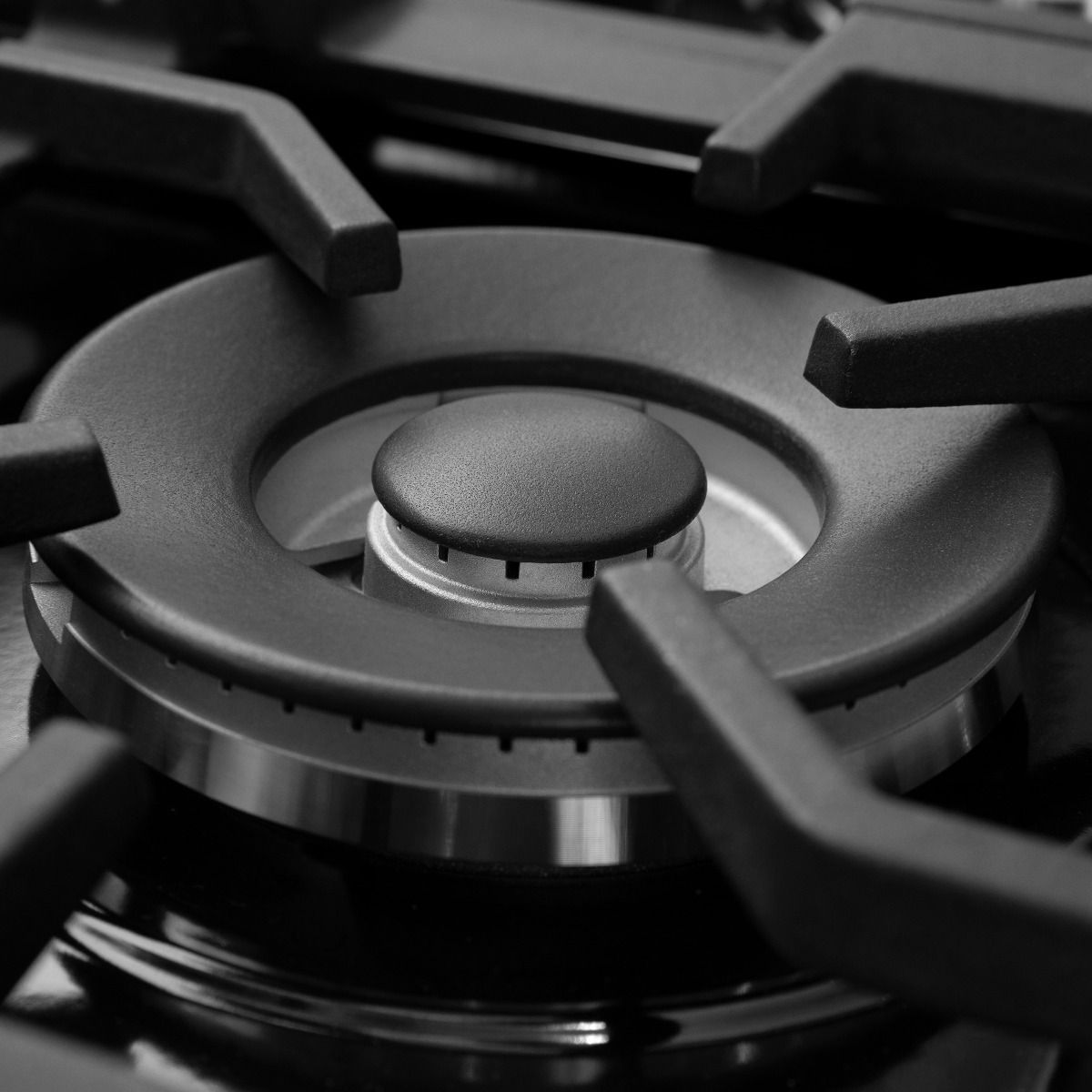 Close-up of black burner cap and ring inside satin stainless steel cooktop