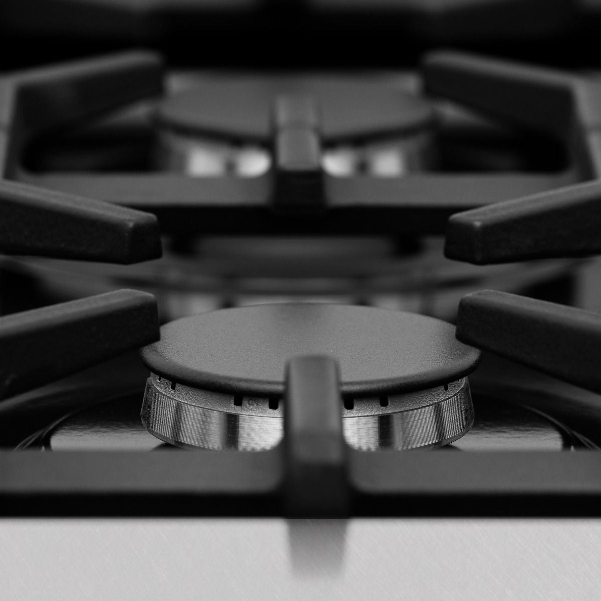 Black gas burner with metal control ring on satin stainless steel cooktop