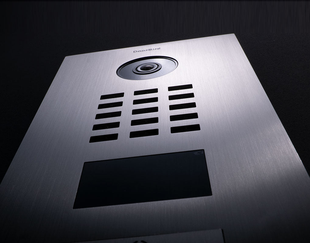 Close-up of stainless steel video door station with camera lens and speaker grille.