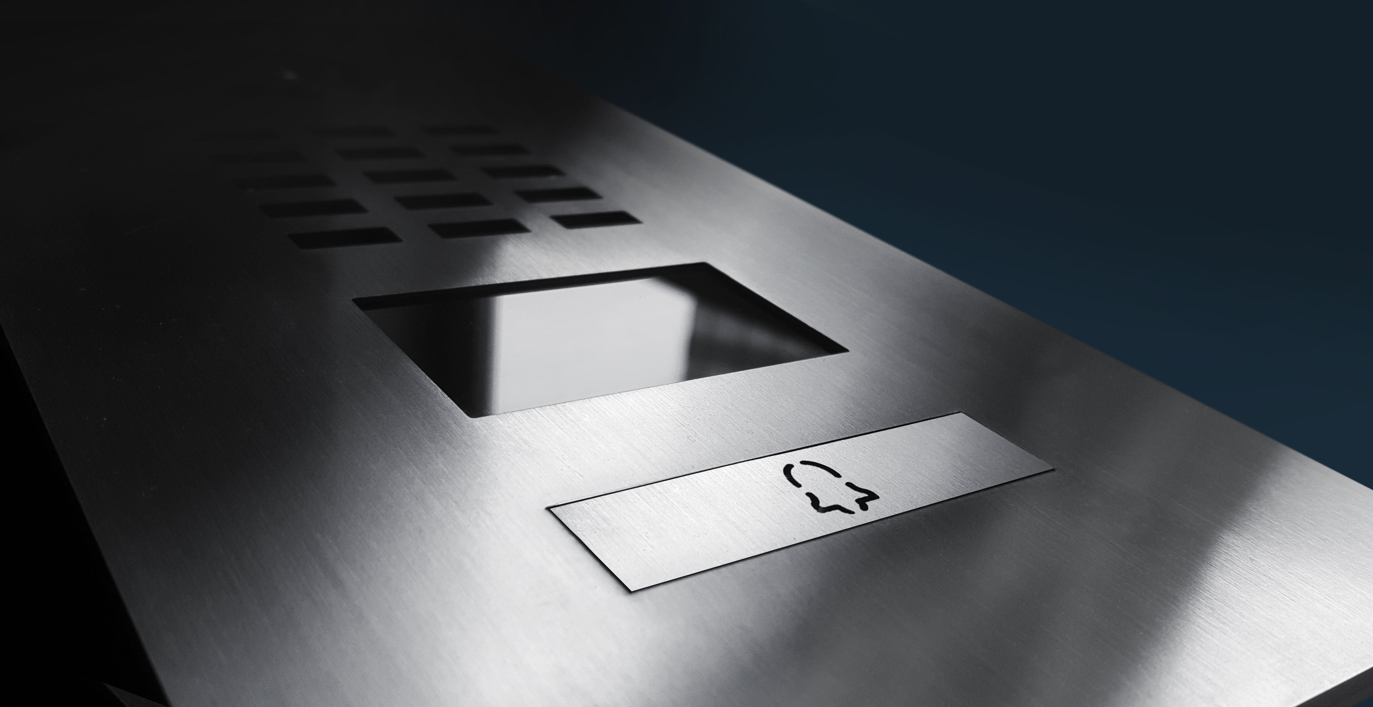 Close-up of brushed metal video door station panel with speaker and label slot.