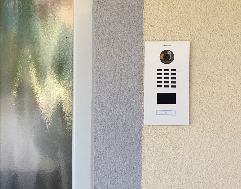 White wall-mounted video door station with camera, keypad, and call button panel