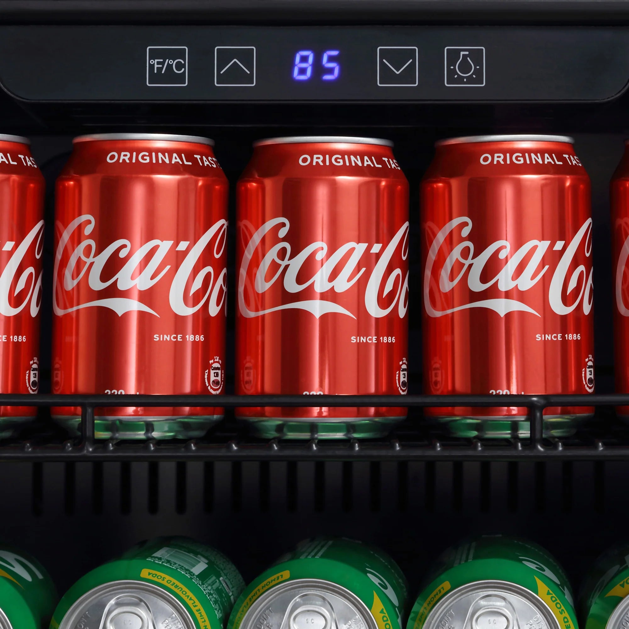 Coca-Cola cans on lower shelf under digital display showing 85°F