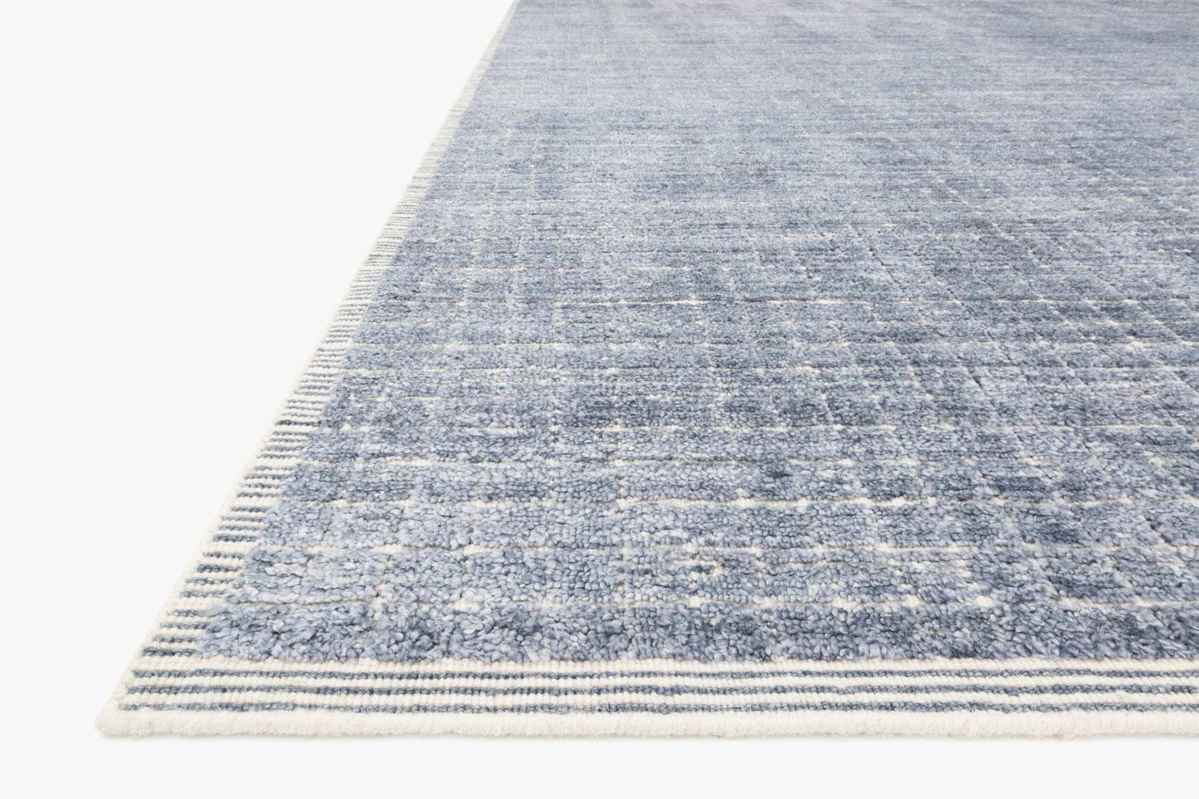 Corner edge of denim blue hand-loomed rug with stitched border and short fringe