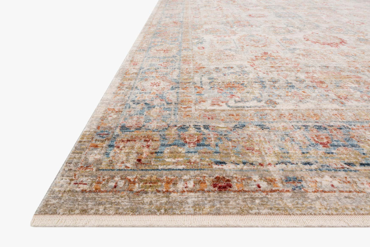 Corner view of ivory and ocean power-loomed rug with faded ornate pattern and fringe edge.