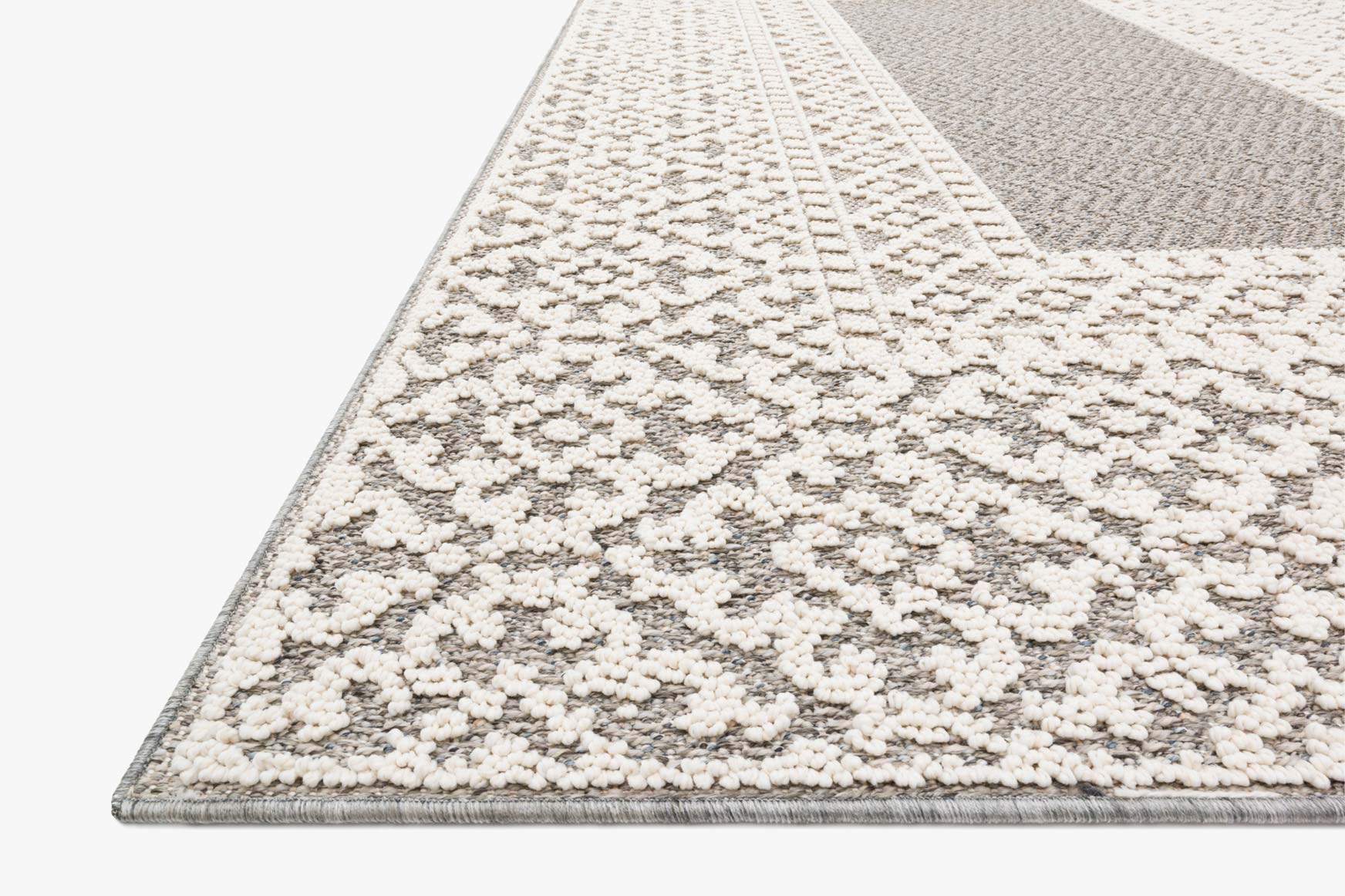 Grey and ivory rug corner with textured pile and repeating floral pattern