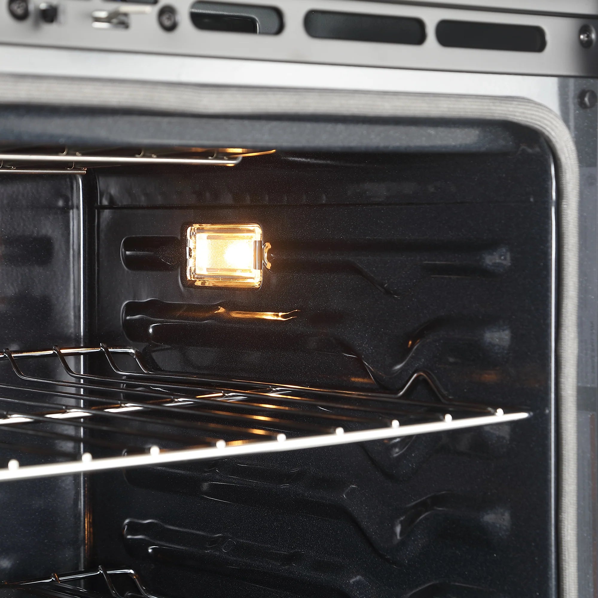 Oven interior with glowing heating element and wire racks inside stainless cavity