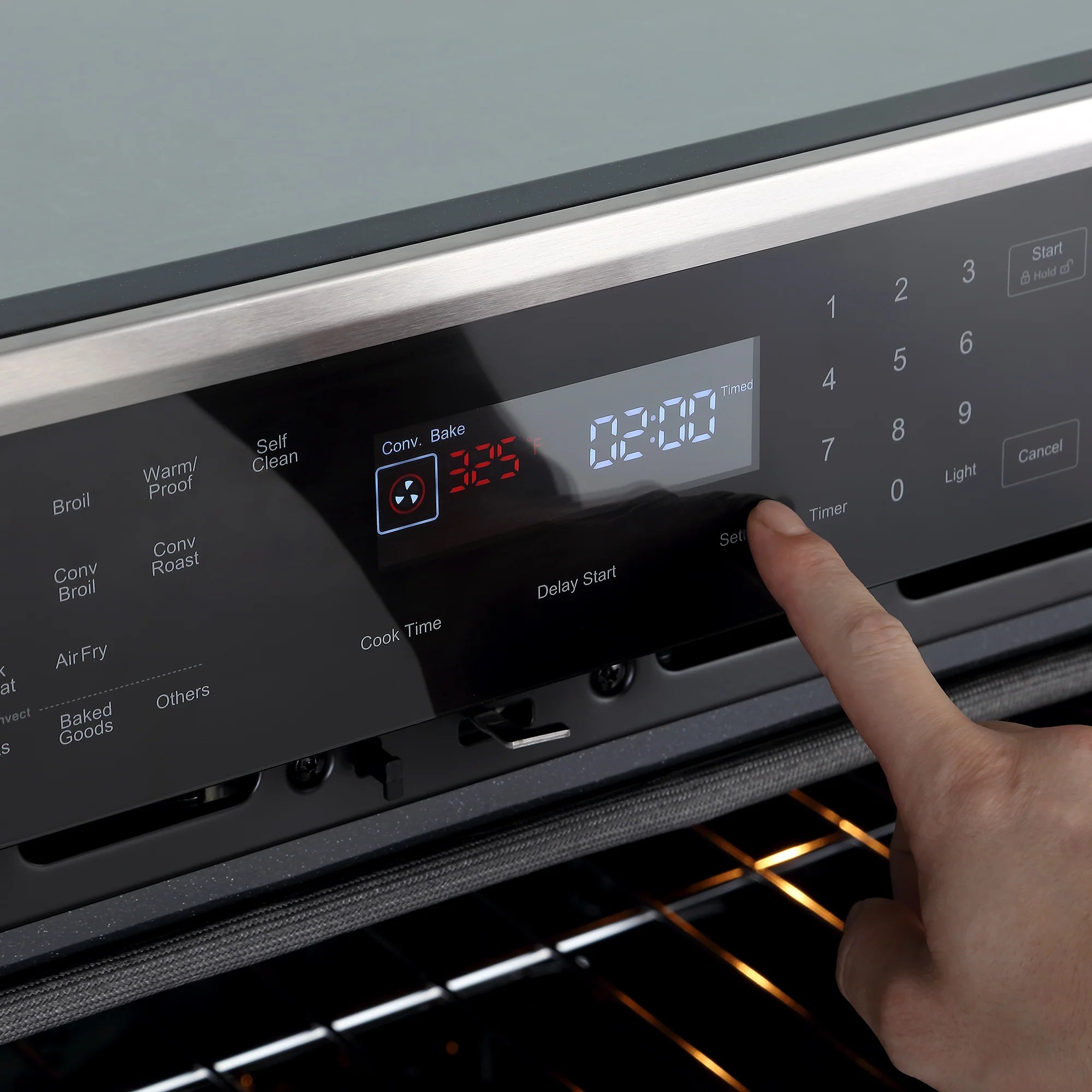 Black oven control panel with digital display and finger pressing keypad