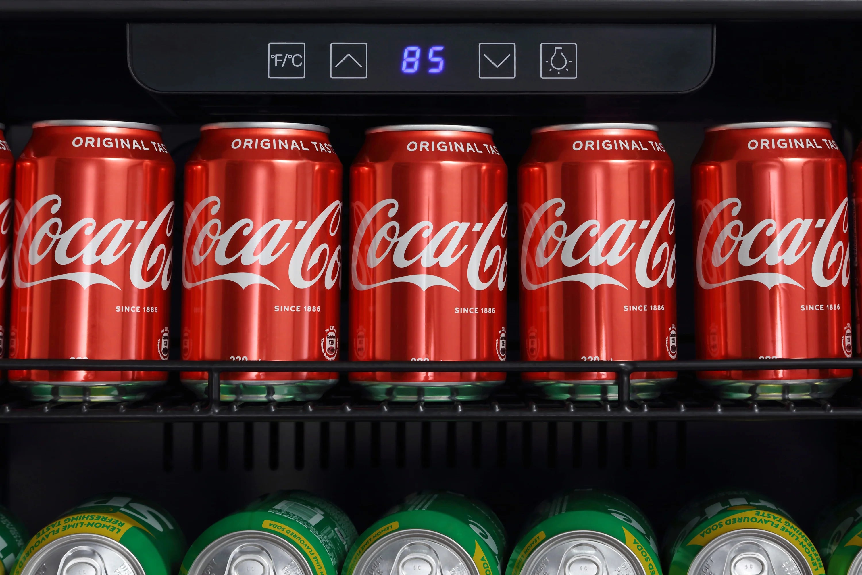 Coca-Cola cans on top shelf with digital control display showing 85°F