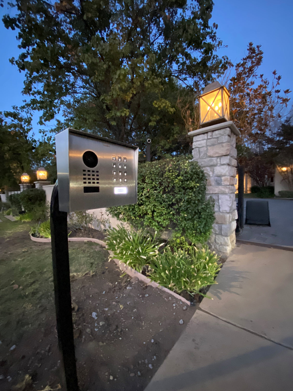 Outdoor stainless steel video door station on a black mount, with camera and keypad