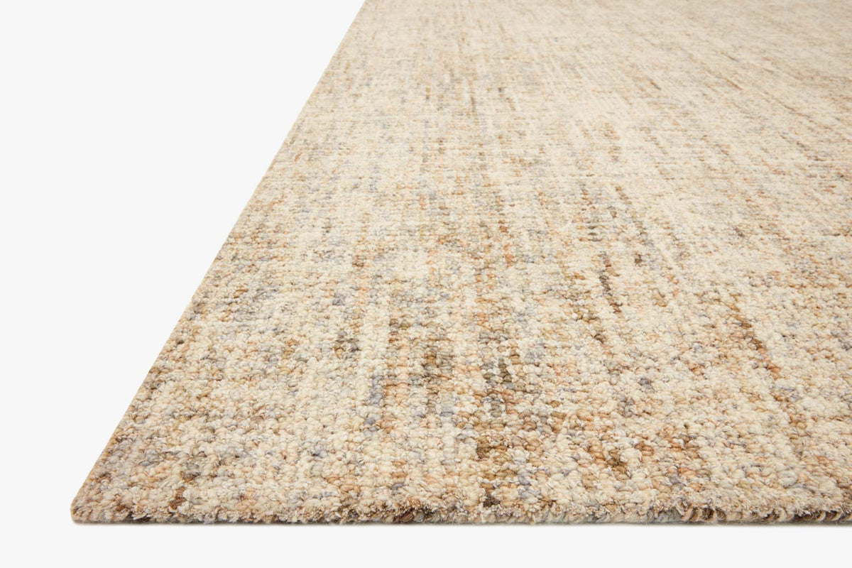 Hand tufted area rug with sand-and-stone speckled texture and angled corner view.
