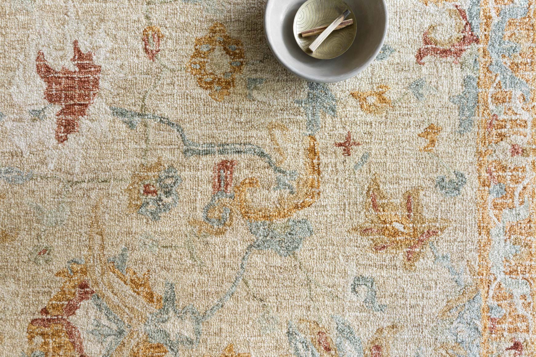 Close-up of ivory hooked rug texture with rust, teal, and brown pattern accents