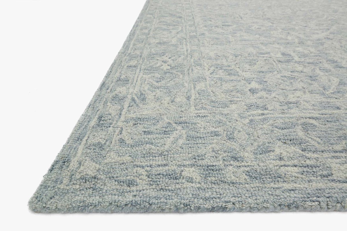 Slate blue hooked rug corner with dense loop texture and geometric pattern border