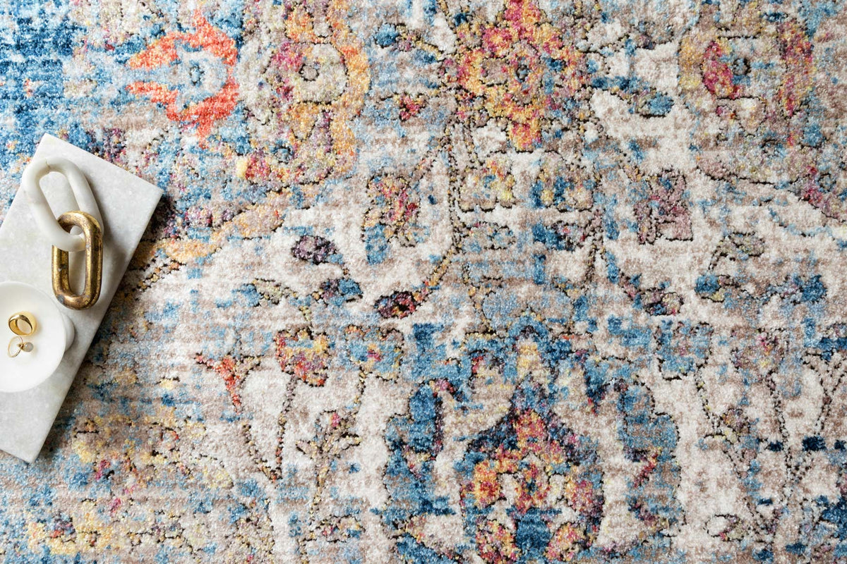 Blue abstract rug close-up with cream, orange, and pink speckled distressed design