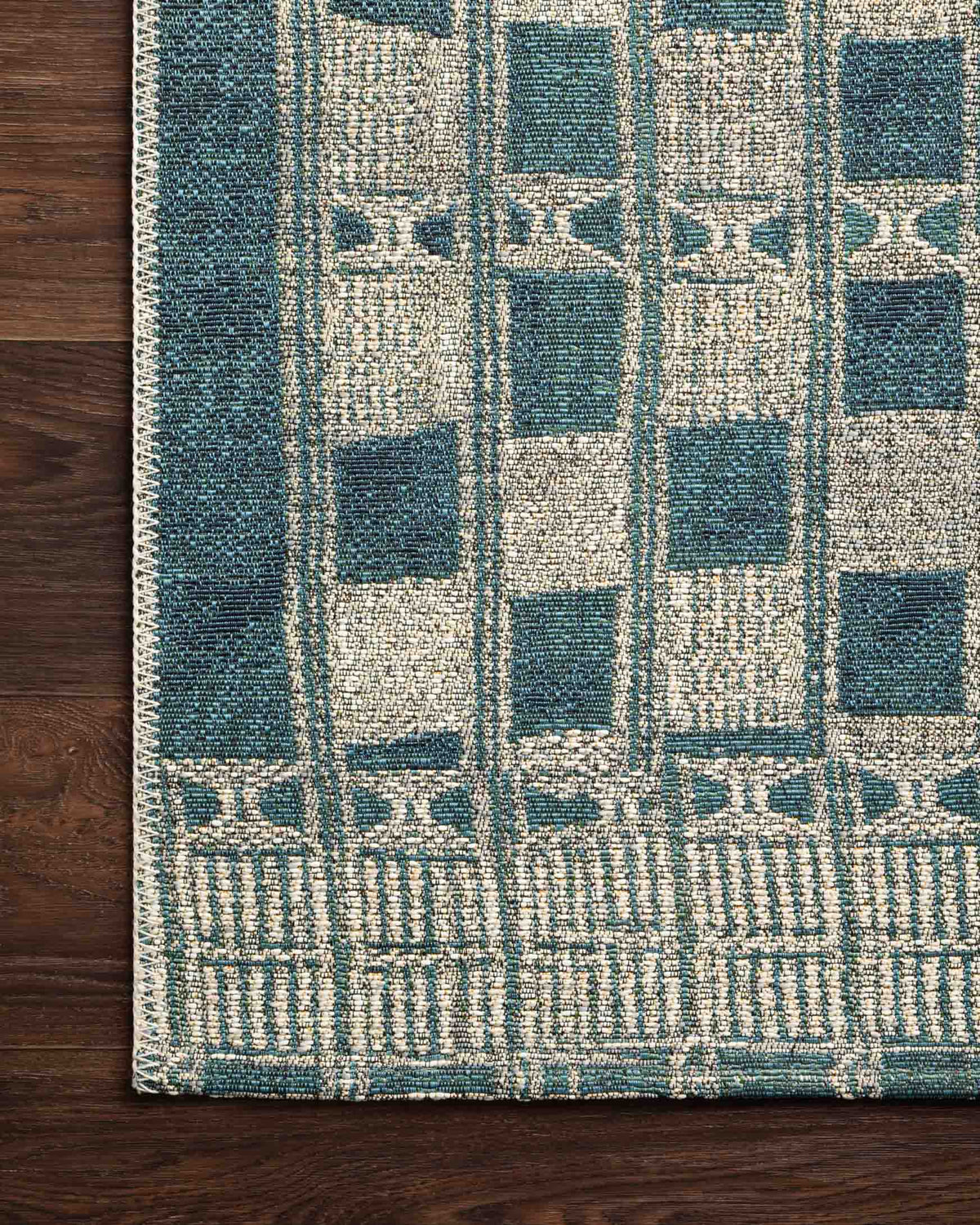 Blue and ivory rug corner with textured check blocks and fringed border