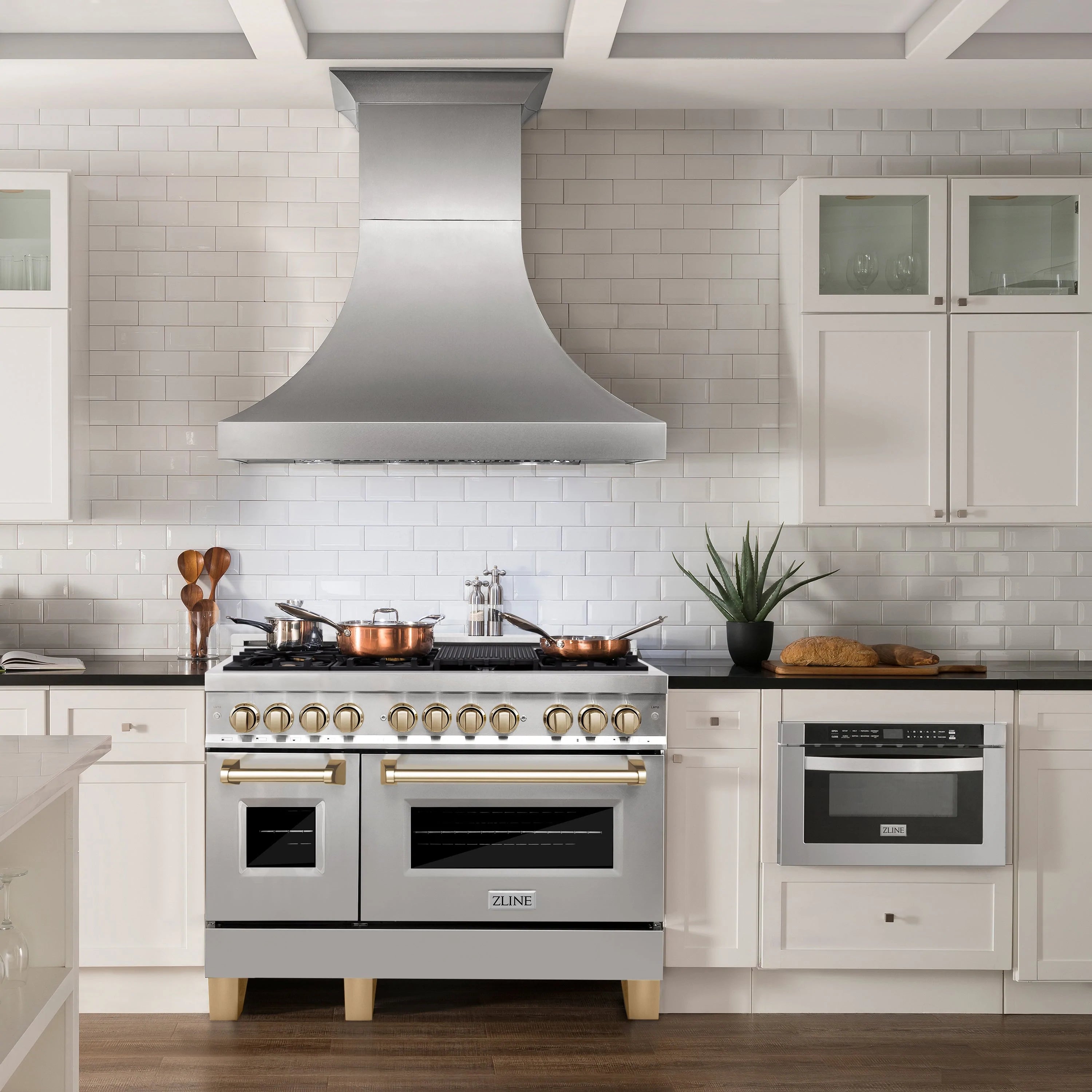 Stainless steel dual fuel range and matching wall hood with gold trim accents