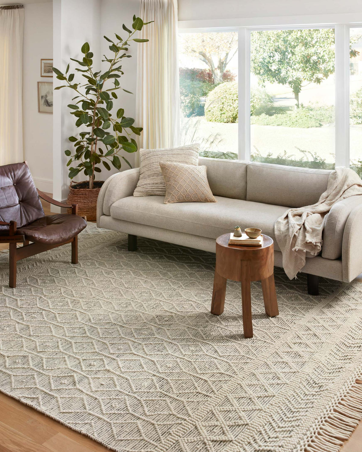 Ivory geometric rug with textured weave and long fringe border, shown on a floor.
