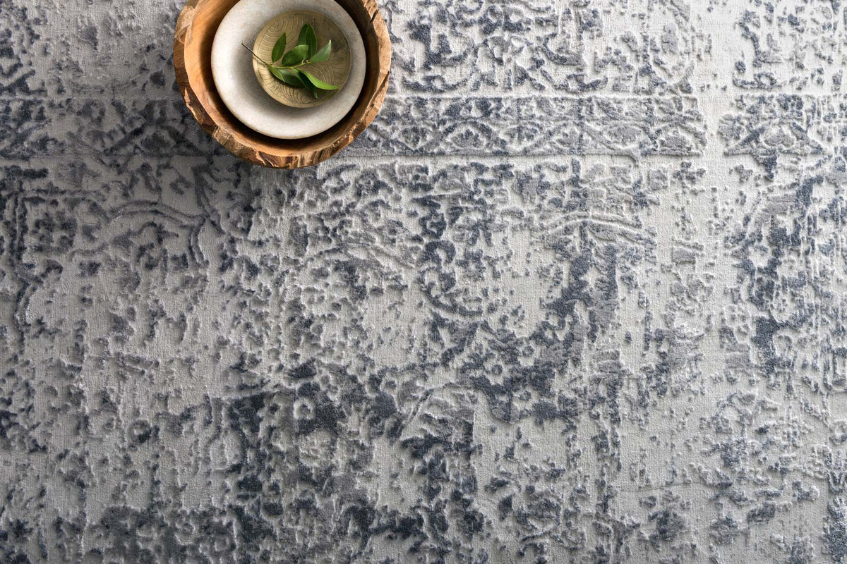 Silver and light gray textured rug with distressed abstract motifs; close-up surface view.
