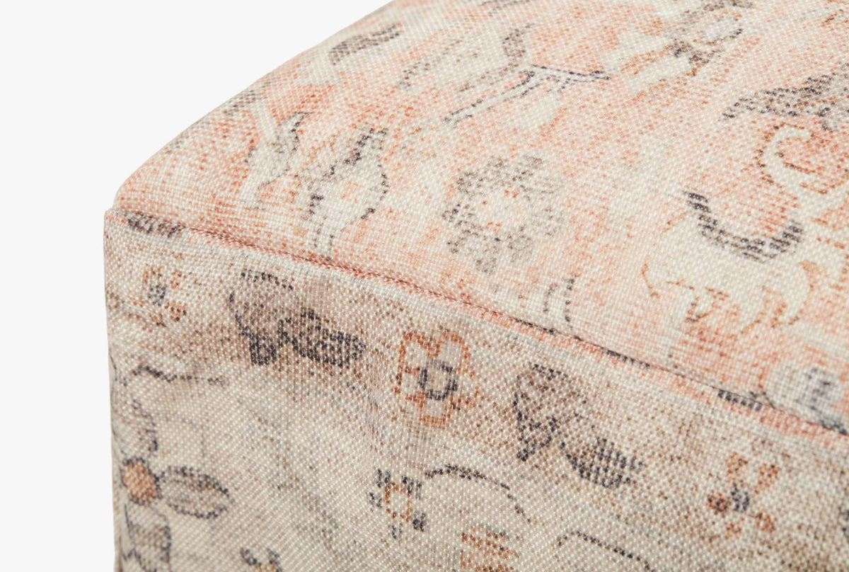 Blush upholstered pouf close-up with patterned fabric texture and stitched edge