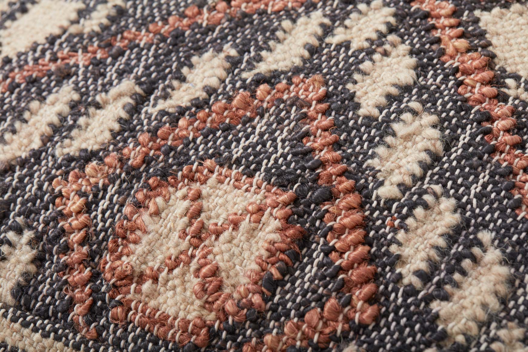 Woven pouf fabric close-up with textured loops and geometric motif in charcoal, cream, rust