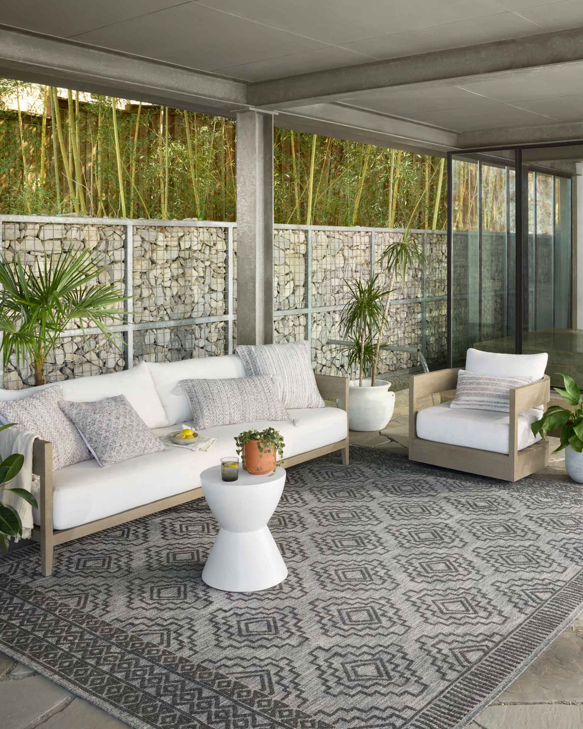 Grey and charcoal geometric rug with diamond motifs and patterned border on floor.