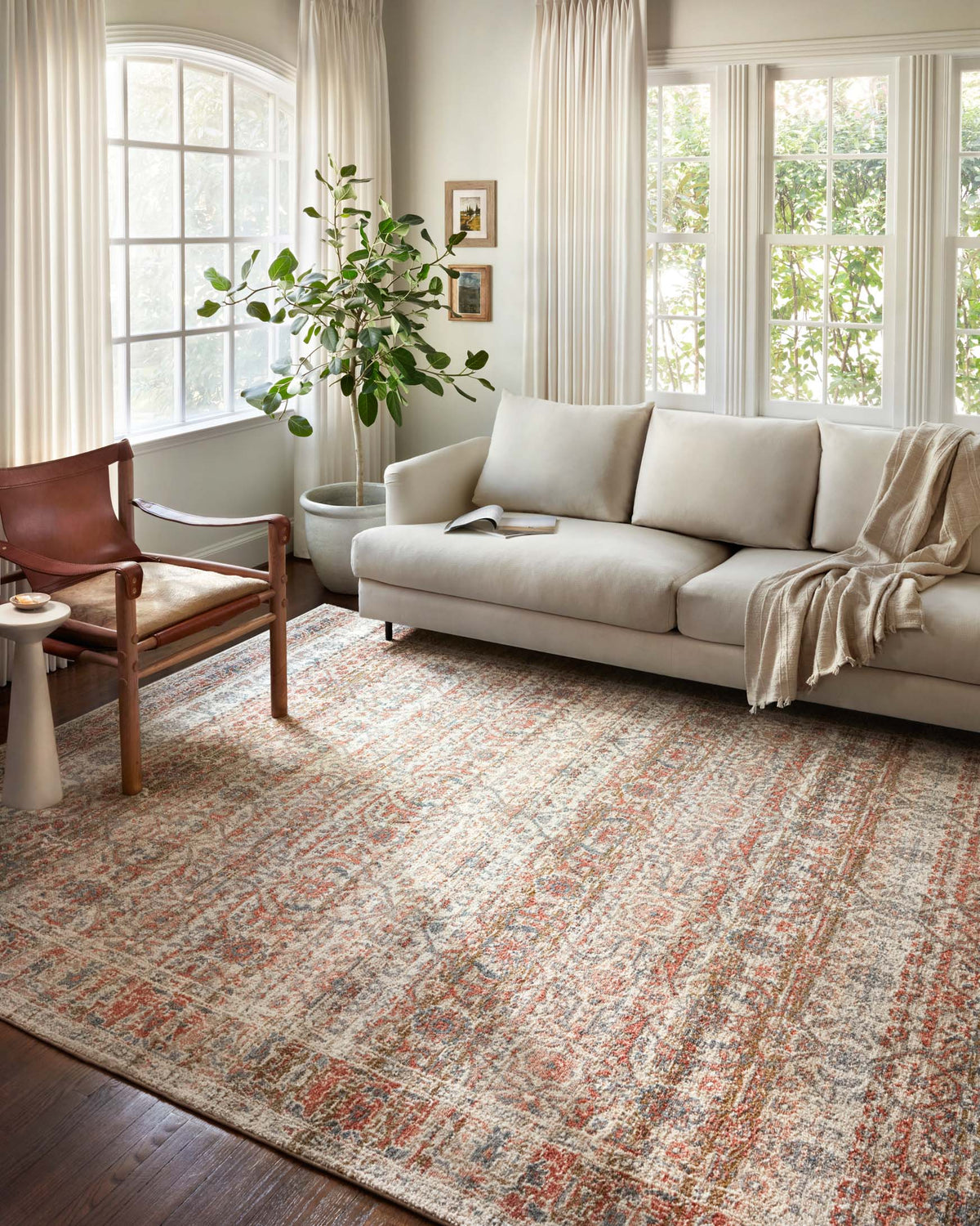 Sand, rust, and blue traditional rug under a living room sofa and curtains