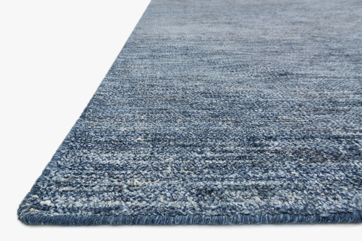 Denim blue hand-knotted rug corner with speckled pile and finished edge
