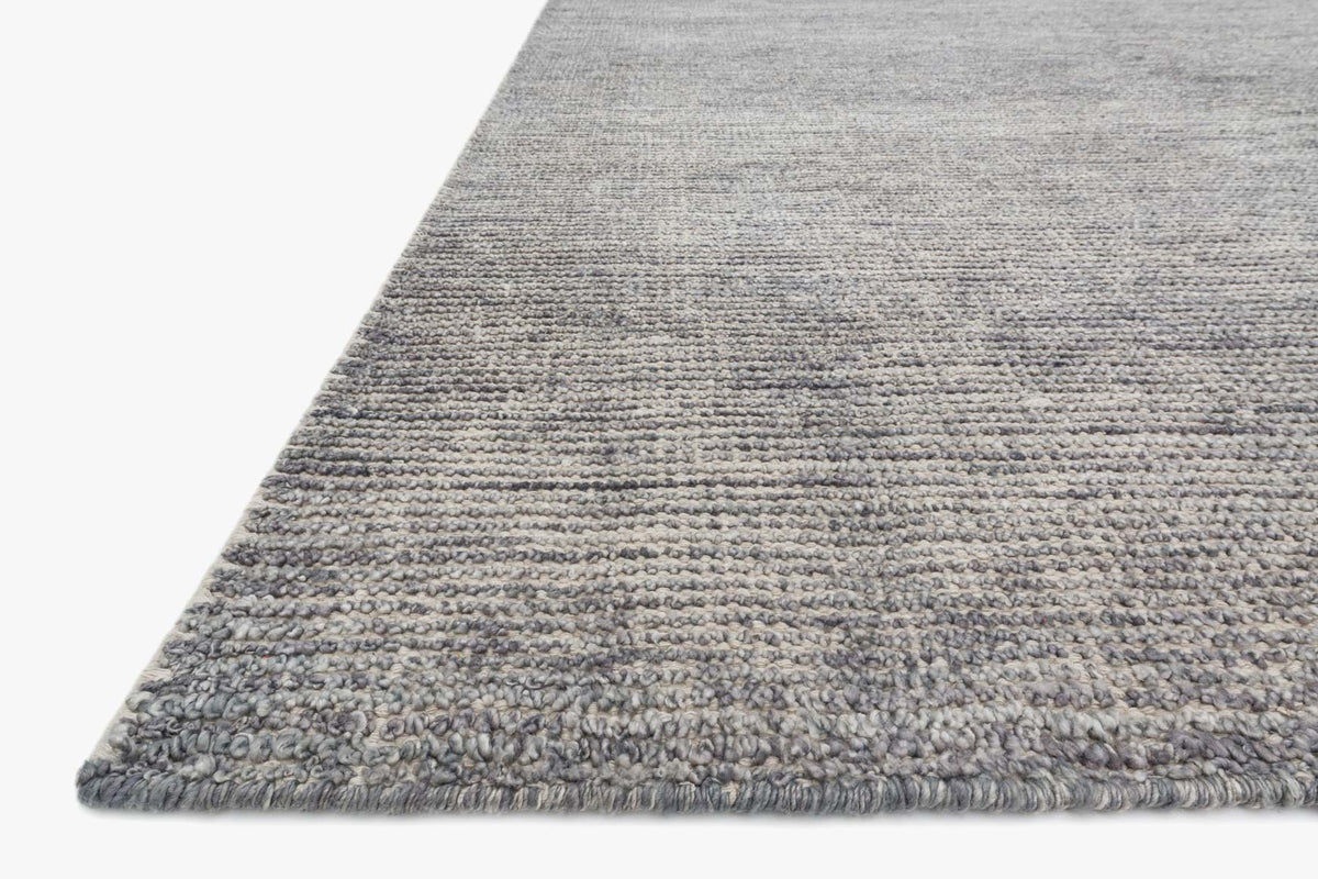 Grey hand-knotted rug corner with fringed border and low-pile weave.