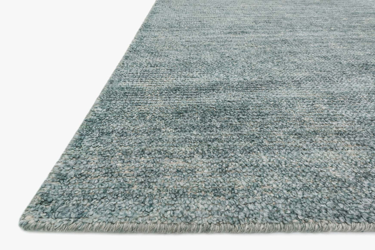 Sea blue hand-knotted rug corner with short fringe and textured speckled surface.