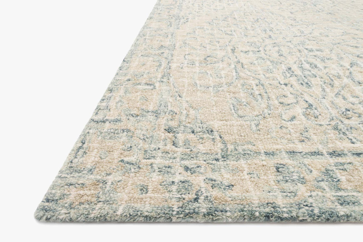 Transitional hooked rug corner with sky-blue and beige abstract motif, angled view
