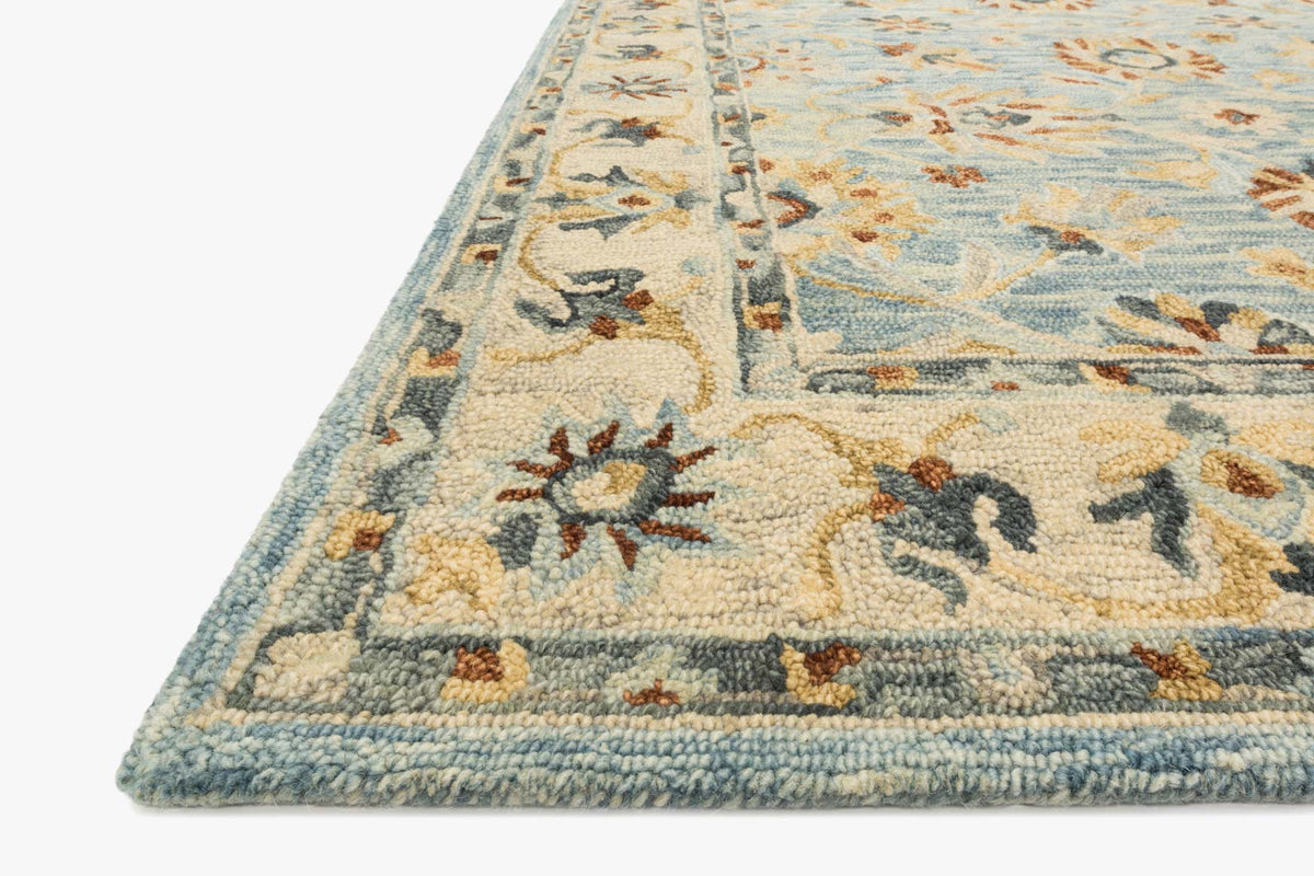 Corner close-up of traditional hooked rug, light blue field with beige floral motifs