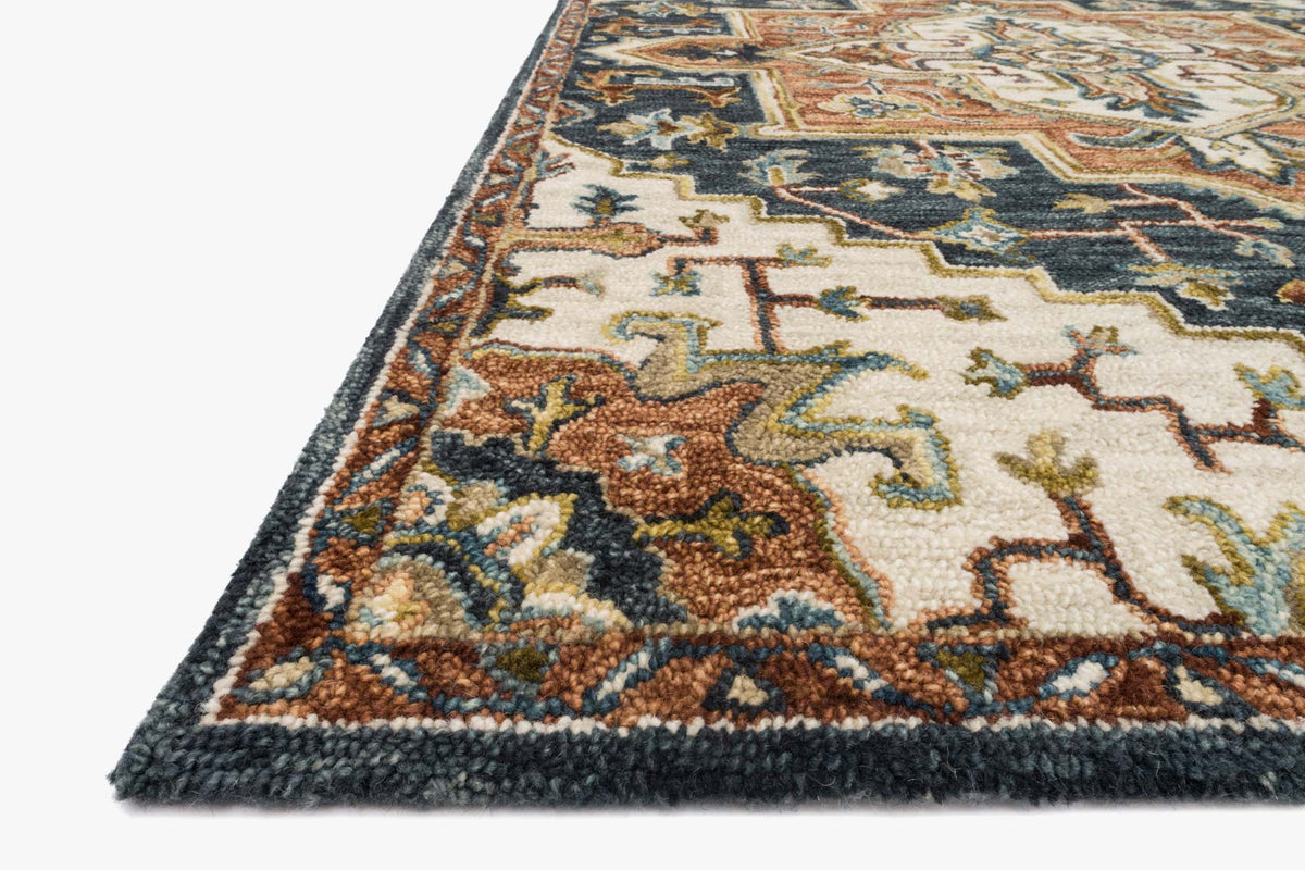 Corner detail of blue hooked rug with ornate pattern and low pile texture, tan and rust