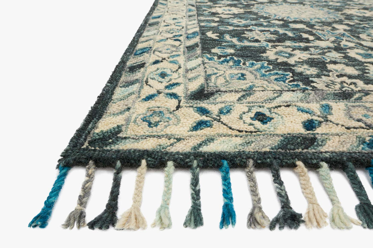 Teal and grey hooked rug corner detail with fringe tassels and floral geometric pattern